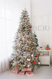 Beautiful christmas tree with toys and gifts in the interior of a bright room at home by the window