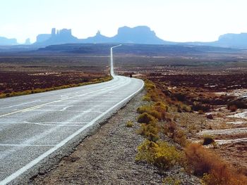 Country road leading towards mountain against sky