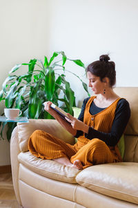 Woman reading book while sitting on sofa at home