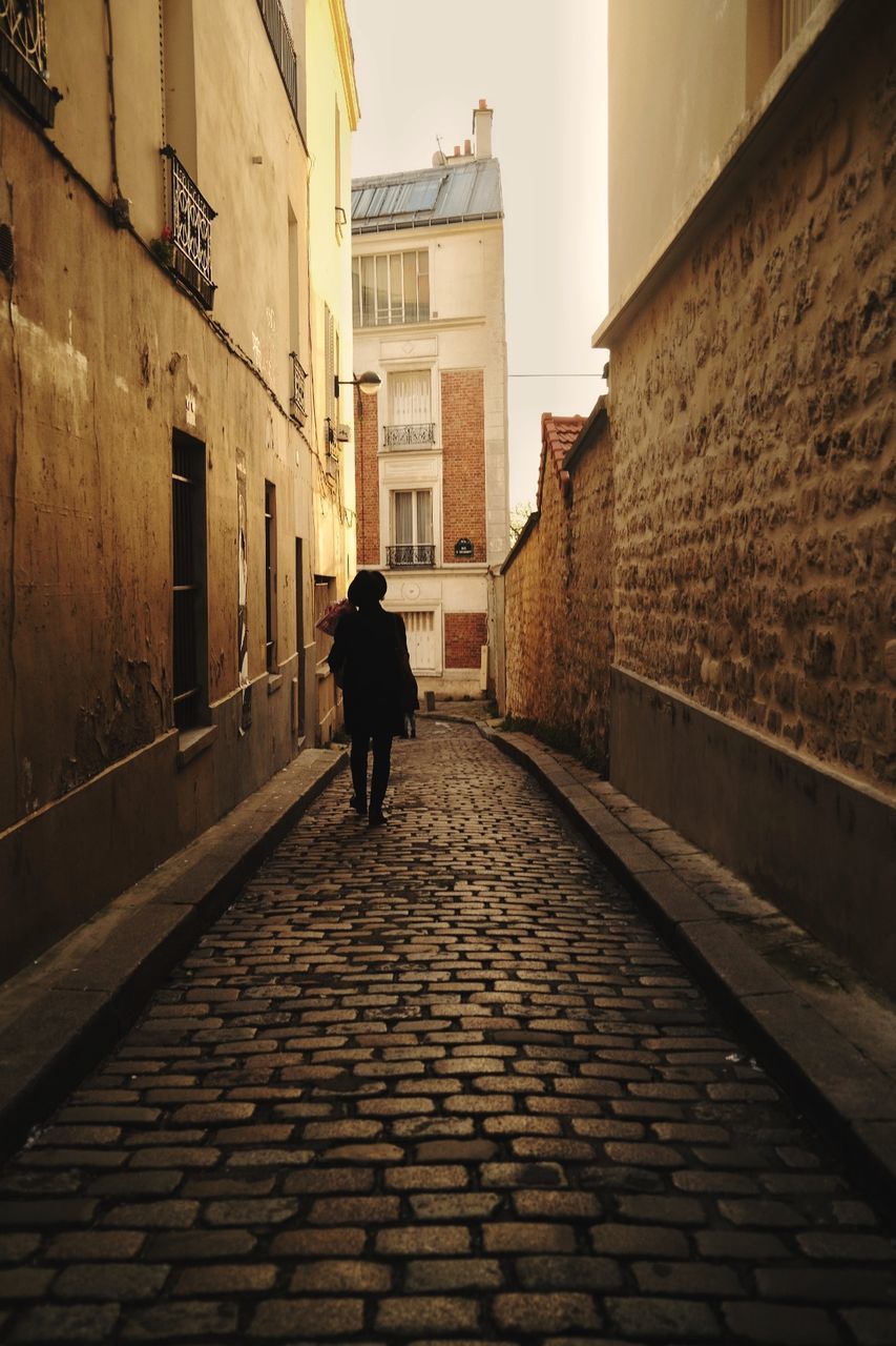 architecture, road, alley, city, street, building exterior, built structure, cobblestone, wall, one person, light, full length, walking, evening, rear view, building, urban area, footpath, darkness, adult, infrastructure, lane, city life, shadow, men, night, the way forward, travel destinations, nature, wood, lifestyles, ancient history, sky, outdoors, travel, residential district, road surface, transportation