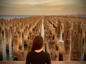 Rear view of woman standing by sea against sky during sunset