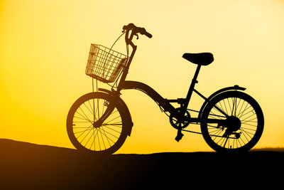 Silhouette person riding bicycle against sky during sunset