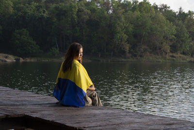 Rear view of woman sitting on rock by lake