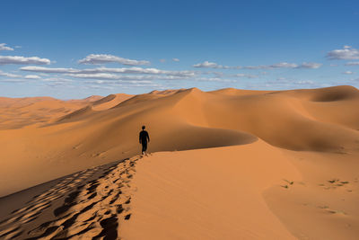 Rear view of man walking at desert against sky
