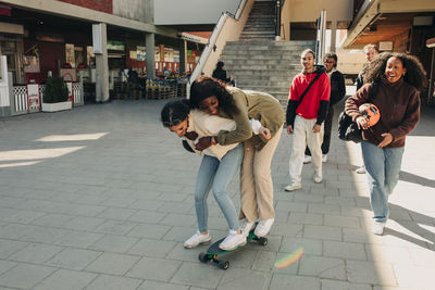 Playful female friends standing on skateboard at street