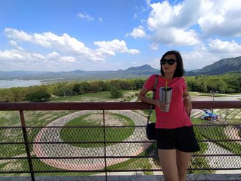 Young woman standing on railing against sky