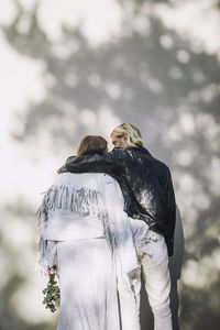 Rear view of groom with arm around bride in front of wall