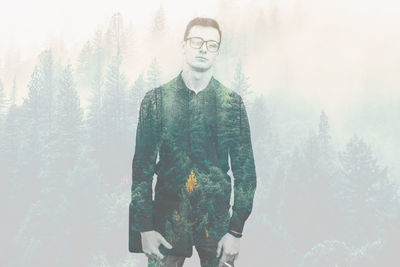 Portrait of young man standing in forest during winter