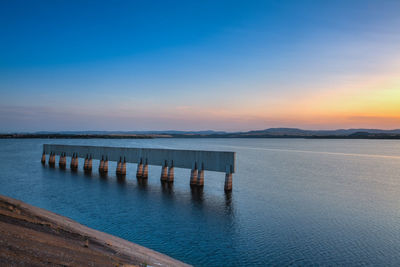 Wooden posts in sea against sky during sunset