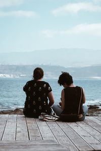 Rear view of friends sitting on pier over sea against sea