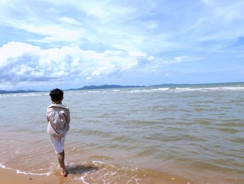 Rear view of man standing on beach against sky