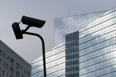 Low angle view of modern office building against sky with security camera