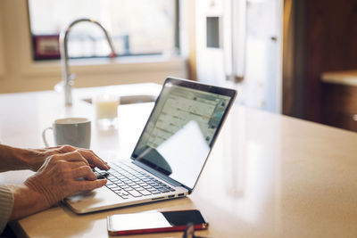 Close-up of senior woman typing on laptop while sitting at kitchen table