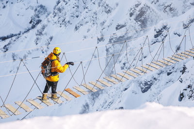 Hiker walking on rope bridge over snow mountains