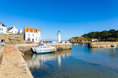 Lighthouse by buildings against clear blue sky