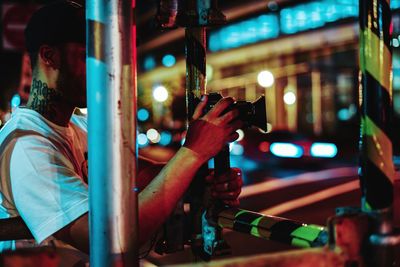 Midsection of man holding illuminated while sitting in city at night