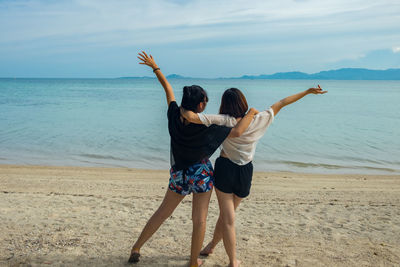 Rear view of women with arms raised standing at beach