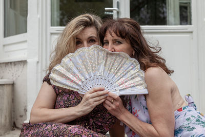 Pair of beautiful middle aged women waving a vintage fan in front of a french villa