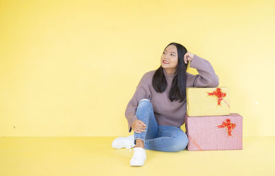 Portrait of smiling young woman sitting against yellow wall