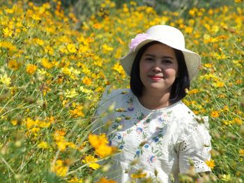 Portrait of beautiful young woman standing by yellow flowering plants