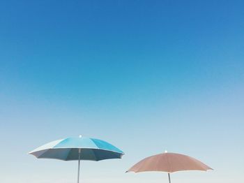 Low angle view of beach umbrellas against clear blue sky