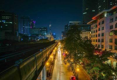 Illuminated street amidst buildings against sky at night