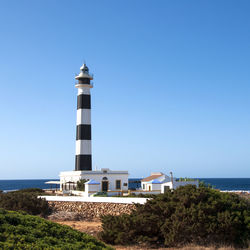 Lighthouse by sea against clear blue sky