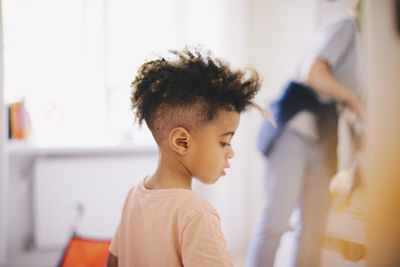 Boy with curly hair looking down while mother working in background