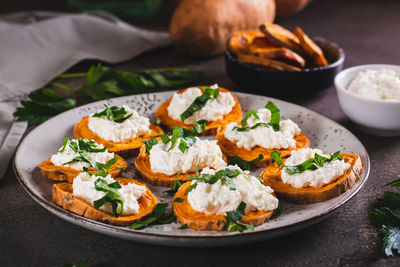 Pieces of baked sweet potato with ricotta and herbs on a plate on the table