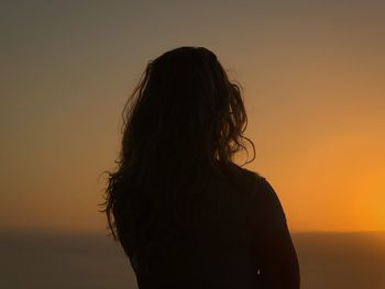 Silhouette woman standing against orange sky during sunset