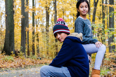 Portrait of smiling siblings on road in forest during autumn