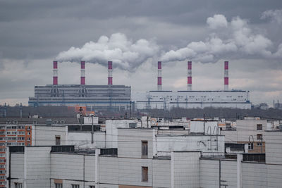 Smoke emitting from factory against cloudy sky