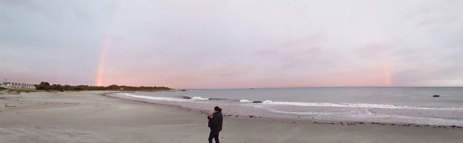 Woman standing at beach against sky during sunset