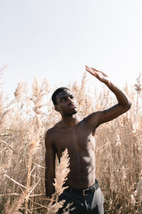 Shirtless young man standing amidst plants on field