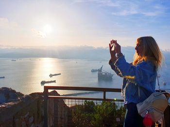 Woman photographing at sea against sky