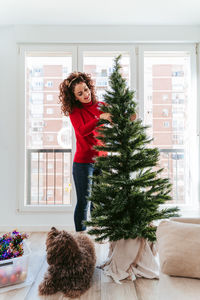 Full length of woman decorating christmas tree at home