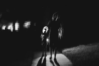 Silhouette mother and son walking on illuminated road at night