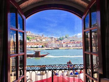 Buildings by sea against sky seen through window