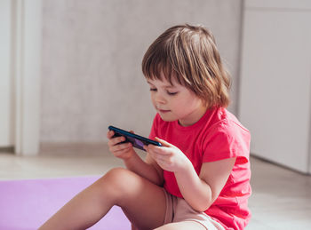 Smiling girl sitting on the floor  and using phone. child playing a video game or watching a video