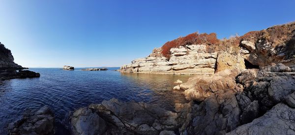 Rock formation in sea against clear blue sky