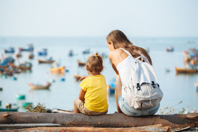 Rear view of boy sitting on sea shore against sky