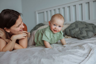 Young mother having fun with one year old son on the bed