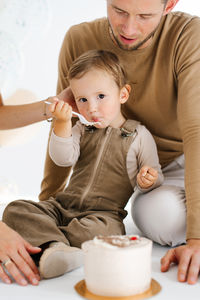 Father and son are sitting on the floor in front of birthday cake. child boy is eating 