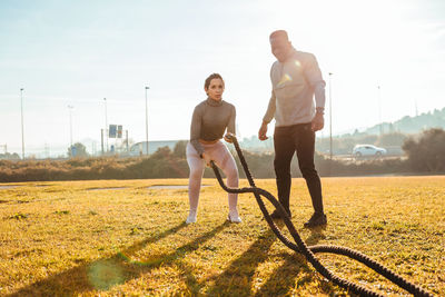 Woman exercising with rope by instructor on land against sky in sunny day