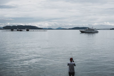 Rear view of man fishing in sea against sky