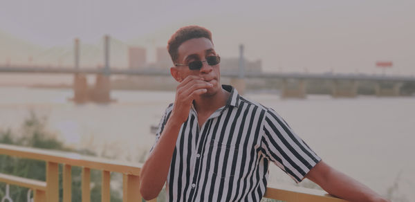 Portrait of young man standing by railing