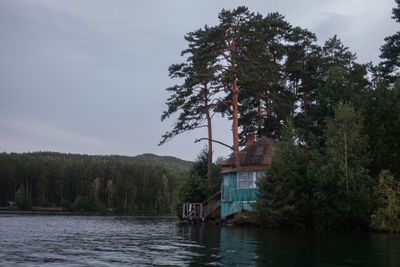 House by lake and trees against sky