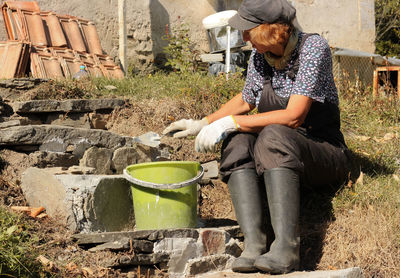 Senior woman working while sitting by cement bucket outdoors