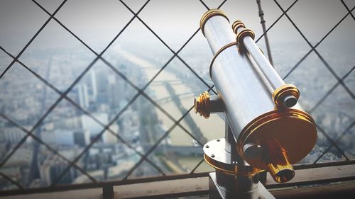 Coin-operated binoculars by chainlink fence in eiffel tower overlooking city