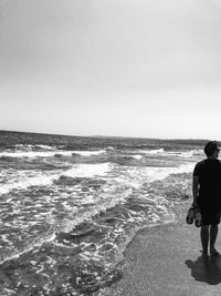 Rear view of man walking on beach against clear sky